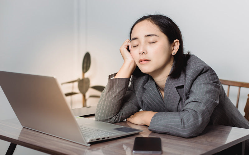 Tired office worker leaning on desk with eyes closed.
