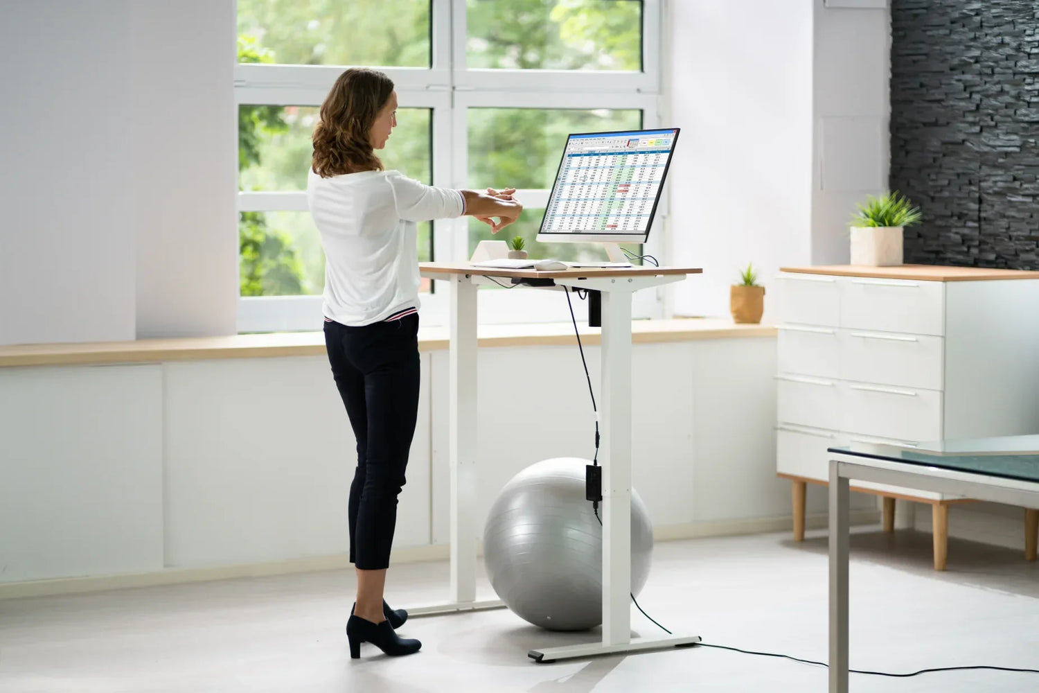 Woman working at a height-adjustable standing office table in Singapore with ergonomic desk setup and monitor.