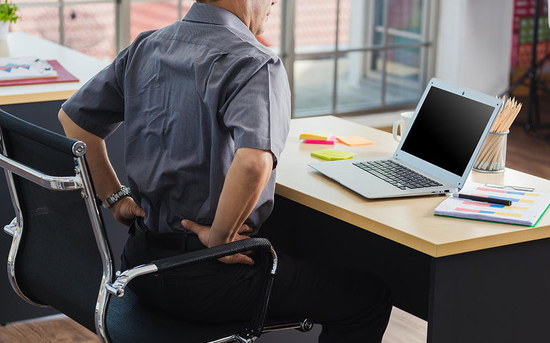Office worker clutching lower back due to uncomfortable sitting posture.