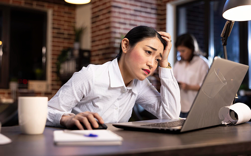 Tired woman leaning on hand while working at laptop.