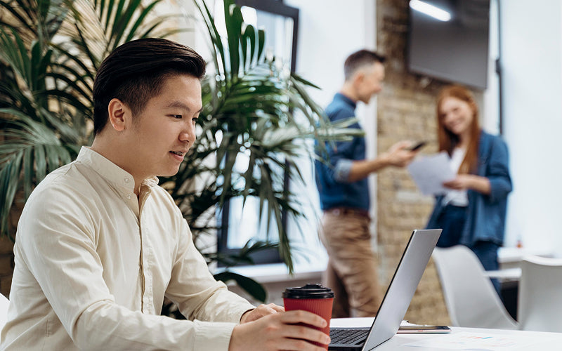 Employee working on laptop in a crowded open office.