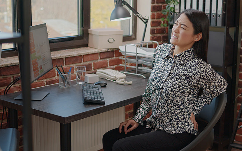 A woman in an office setting experiencing lower back pain