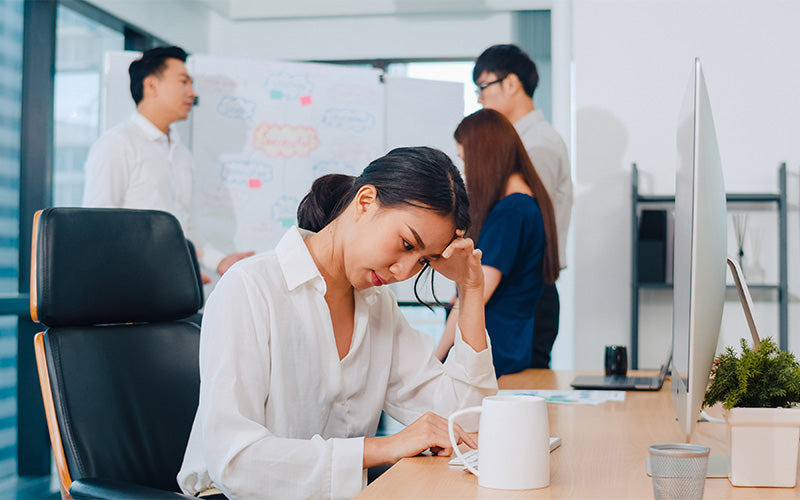 A stressed office worker leaning over her desk with her head in her hand