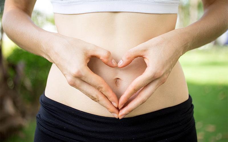 Hands form heart shape over stomach outdoors.