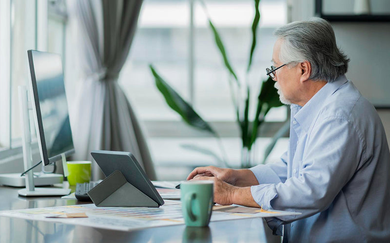 Senior man using computer with poor posture at desk.