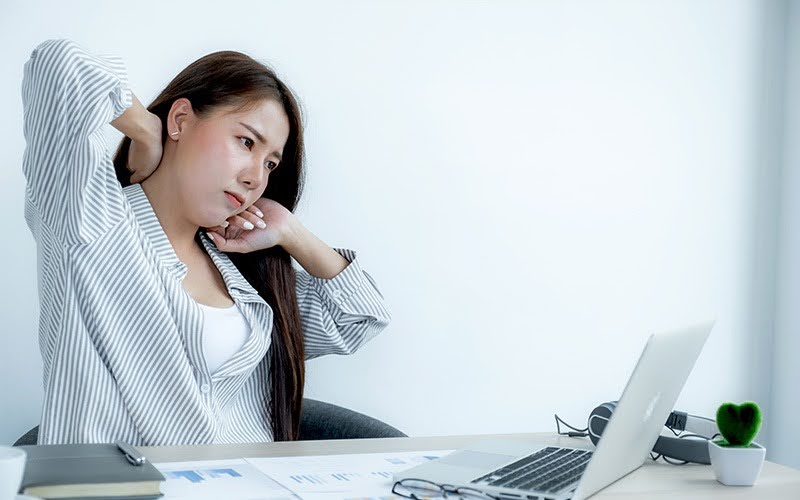 Woman at desk rubbing her stiff neck in discomfort.