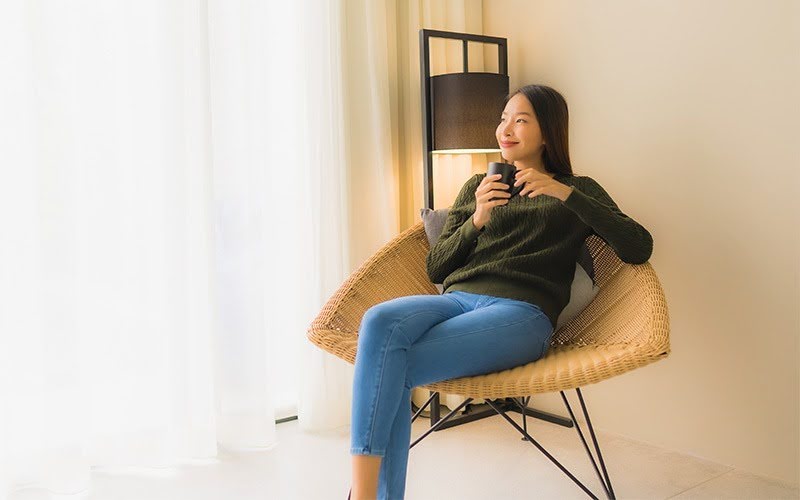 Woman sitting cross-legged in a woven armchair.