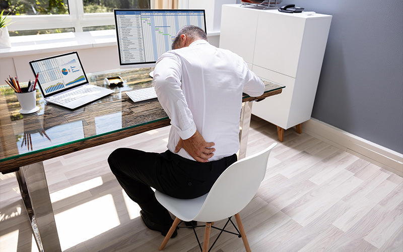 Businessman leaning over office desk holding his painful lower back.