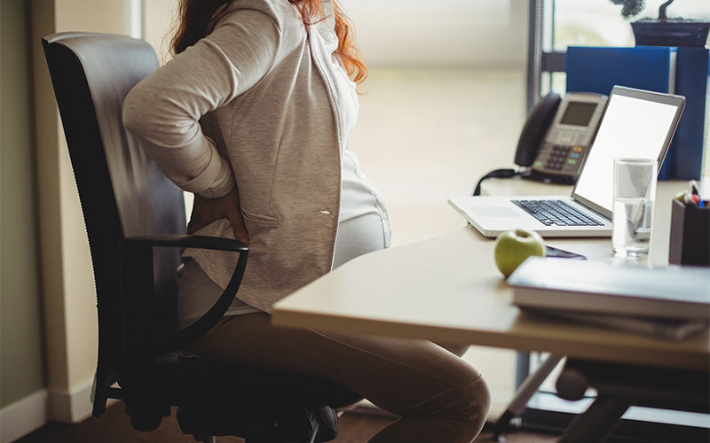 Pregnant woman experiencing lower back fatigue from office sitting.